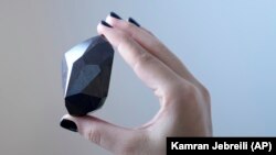 An employee of Sotheby's Dubai holds a 555.55 Carat Black Diamond called "The Enigma." Photo taken at Sotheby's Dubai gallery in Dubai, United Arab Emirates, January 17, 2022. (AP Photo/Kamran Jebreili)