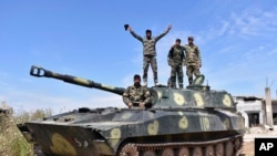 FILE - In this photo released by the Syrian official news agency SANA, Syrian army soldiers flash the victory sign as they stand on their tank in the village of Kfar Nabuda, in the countryside of Hama province, Syria, May 11, 2019.