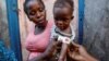 Cherlande Dolcine, 20, holds her daughter Dainaika Jean, 2, in front of their house as a measurement shows red for severe malnourishment in Port-de-Paix, Haiti, Jan. 30, 2020. 