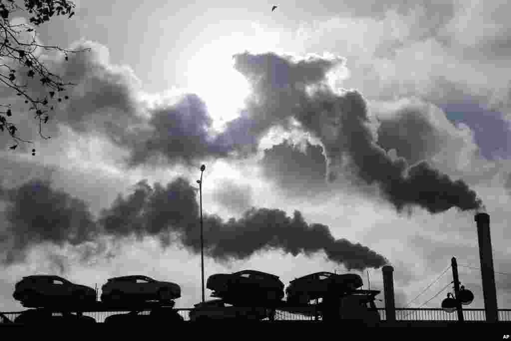 FILE - Smoke rises from a factory as a truck loaded with cars crosses a bridge in Paris, France, Nov. 30, 2018.