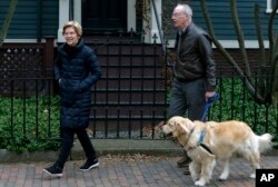 Democratic Sen. Elizabeth Warren steps outside her home with her husband Bruce Mann, right, and their retriever Bailey, Dec. 31, 2018, in Cambridge, Massachusetts, where she confirmed that she is launching an exploratory committee to run for president.