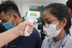 A local journalist, right, has her temperature checked to cover a handover ceremony of a donation in Phnom Penh, Cambodia, Saturday, March 28, 2020. (AP photo)