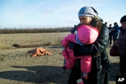Seorang perempuan dan anaknya serta orang-orang lain lagi melewati mayat seorang pria yang tewas akibat ranjau darat dekat tempat penyeberangan ke daerah yang dikuasai pemerintah Ukraina, dekat Donetsk, Ukraina (10/2).