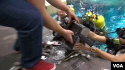 A diver hands a device to a West Virginia student. (G. Flakus/VOA)