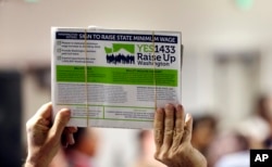 FILE - A supporter holds up a petition for Initiative 1433, a ballot measure to raise Washington state’s minimum wage and allow all workers in the state to earn paid sick leave, March 22, 2016, in Everett, Wash.