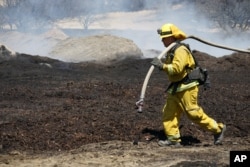 Firefighters water down scorched compost material at a property burned near Phelan, Calif., Aug. 19, 2016.