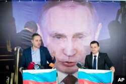 Russian opposition activists Ilya Yashin, right, and Vladimir Milov present their report "Putin. Results. 2018" in front of a poster displaying Russian President Vladimir Putin in Moscow, Russia, Wednesday, March 14, 2018