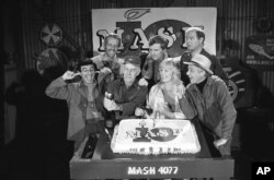 FILE - Cast members of the "M.A.S.H." television series Jamie Farr, from front left, Harry Morgan, Loretta Swit, William Christopher and, from back left, Mike Farrell, Alan Alda and David Ogden Stiers celebrate during a party on the set of the popular CBS program in Los Angeles, Oct. 22, 1981.