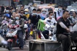 FILE - In this file photo dated Friday, July 2, 2021, people riding bicycles and scooters wait to cross an intersection during rush hour in Beijing. (AP Photo/Mark Schiefelbein, FILE)