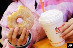 FILE - A girl has a doughnut and a beverage in New York, Feb. 14, 2013. A new study finds more than half the calories consumed in the average American diet comes from "ultra-processed" foods, including sugary drinks.
