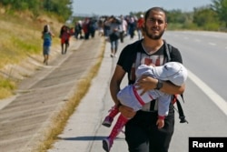 FILE - A Syrian migrant carries a baby as he walks towards the Greece border on a road near Edirne, Turkey, Sept. 15, 2015.
