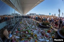 Flight attendants and mourners gather near flower bouquets as they pay their respects at Schiphol Airport during a national day of mourning for the victims of the downed Malaysia Airlines flight MH17, in Schiphol July 23, 2014.