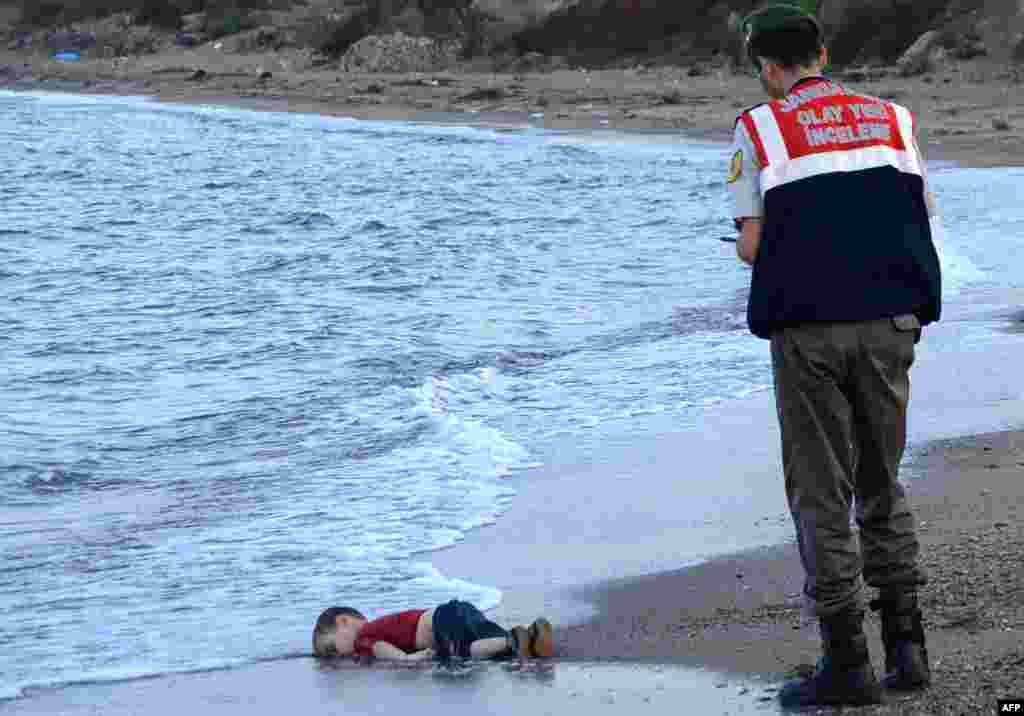 A Turkish police officer stands next to a migrant child&#39;s dead body (Aylan Shenu) off the shores in Bodrum, southern Turkey, on Sept. 2, 2015 after a boat carrying refugees sank while reaching the Greek island of Kos.