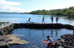 FILE - A woman washes clothes as children play near the water on the island of SavaiÕi, Samoa, July 16, 2019.
