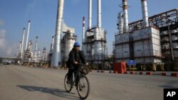 FILE - Iranian oil worker rides his bicycle at the Tehran's oil refinery south of the capital Tehran, Iran.
