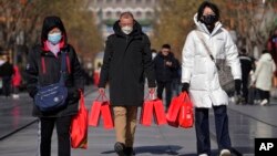 FILE - People wearing face masks carry shopping bags as they walk down Qianmen Street, in Beijing, Jan. 17, 2023. 