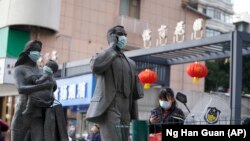 资料照片：中国武汉市，一名女子正走过带着口罩的雕塑面前。期间，世卫组织新冠溯源专家小组正在武汉考察。（2021年1月29日）