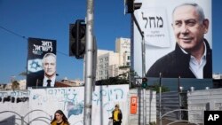Para pejalan kaki melewati poster kampanye Partai Likud yang dipimpin Perdana Menteri Israel Benjamin Netanyahu (kanan) dan Partai Biru dan Putih, pimpinan Benny Gantz (kiri) di Bnei Brak, Israel, 1 Maret 2020. (Foto: AP)