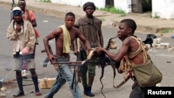 FILE - May 8, 1996 photo shows a street fighter with Charles Taylor's NPFL firing his machine gun while holding the string of bullets in his teeth during a heavy exchange.