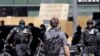 A protester holds up a sign toward police officers Sunday, July 26, 2020, in Seattle, where a small group of demonstrators gathered to protest against Immigration and Customs Enforcement.