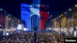 Revelers gather near the Arc de Triomphe, lit in the colors of the French flag, on the Champs Elysees in Paris during New Year's celebrations, Dec. 31, 2015.