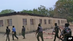 FILE - Security guards walk past a burned-out government secondary school in Chibok, Nigeria. April 21, 2014.