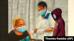 A man wearing a face covering to prevent the spread of coronavirus, walks past a painting supporting COVID-19 vaccinations in Duduza, east of Johannesburg, South Africa, Wednesday, June 23, 2021. (AP Photo/Themba Hadebe)