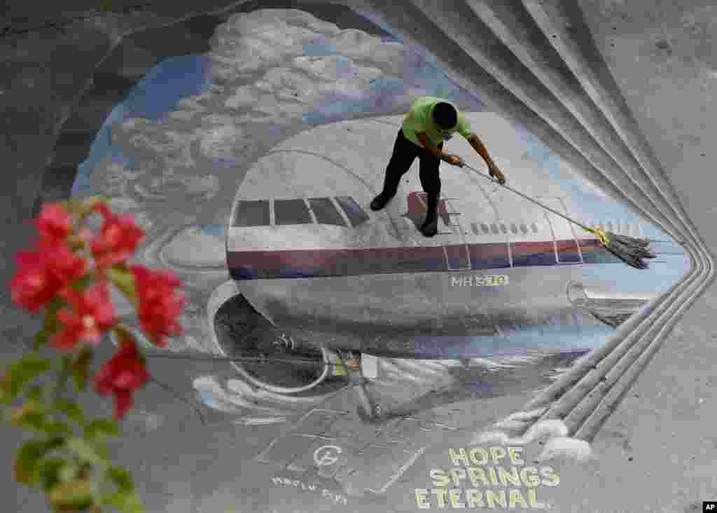 Seorang pekerja membersihkan gambar mural pesawat Malaysia Airlines Flight 370 di sekolah Benigno &quot;Ninoy&quot; Aquino di kota Makati, Filipina.