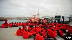 Des migrants sub-sahariens assis sur une clôture métallique entre le Maroc et l'enclave espagnole de Melilla, discutent avec un officier de la Guardia Civil espagnole tenant un bâton, le jeudi 1er mai 2014