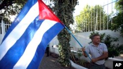 FILE - A man waves a Cuban flag while celebrating the restoration of diplomatic relations between Havana and Washington, in the courtyard of the Cuban Embassy in Santiago, Chile, Dec. 17, 2014.