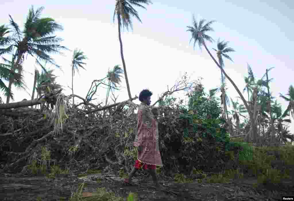 A woman carrying her baby walks past fallen trees on the southern island of Tanna, where residents told relief workers they were running low on food and other basic supplies, March 18, 2015. 