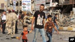 Warga melewati lokasi ledakan bom mobil di Baghdad (16/10). (AP/Khalid Mohammed)