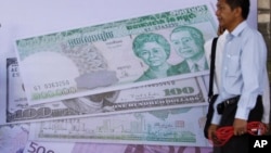 Cambodian men stand near local and international currencies poster during an inauguration ceremony of the Cambodia Securities Exchange in Phnom Penh, file photo. 
