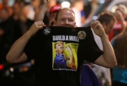 FILE - A Donald Trump supporter holds up his shirt, which bears the slogan "Build a Wall," at a campaign rally for Trump, Aug. 30, 2016, in Everett, Wash.