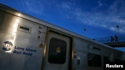 FILE - A Long Island Railroad train is seen parked as commuters make their way over a foot bridge in Port Washington, New York.