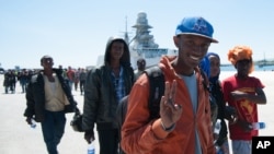 FILE - A migrant flashes the victory sign after disembarking from an Italian navy vessel at the port of Augusta, Sicily, in April. A new report highlights the potential economic benefit of migrants to host countries.