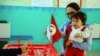 FILE - A woman casts her vote with her child during the first round of the Tunisian presidential election in a polling station at Marsa, outside Tunis, Nov. 23, 2014. The vote was another step forward in Tunisia's peaceful transition to democracy.