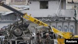 Petugas keamanan Afghanistan berdiri di dekat kendaraan yang hancur akibat ledakan bom di Kabul, Afghanistan (19/4).