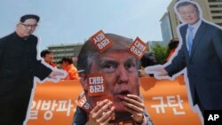 A protester wearing a mask of U.S. President Donald Trump performs with cut-out photos of North Korean leader Kim Jong Un and South Korean President Moon Jae-in, right, during a rally in Seoul, South Korea, May 25, 2018. 