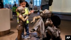 FILE - A boy pats the head of a sculpture of a Neanderthal boy, inside the Smithsonian Hall of Human Origins, Thursday, July 20, 2023, at the Smithsonian Museum of Natural History in Washington.(AP Photo/Jacquelyn Martin)