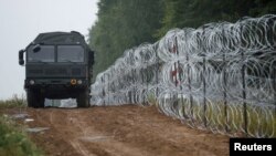 FILE - A view of a vehicle next to a fence built by Polish soldiers on the border between Poland and Belarus is seen near the village of Nomiki, Poland, Aug. 26, 2021.