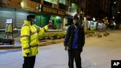 FILE - A Kenyan police officer stops a man who was heading home past the start of the daily dusk-to-dawn curfew in the Eastleigh area of Nairobi, Kenya, May 6, 2020.
