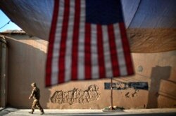 FILE - A U.S. soldier walks past an American flag hanging in preparation for a ceremony marking the 10th anniversary of the 9/11 attacks, at Forward Operating Base Bostick, in Kunar province, Afghanistan, Sept. 11, 2011.