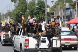 FILE - Taliban fighters wave as they patrol in a convoy along a street in Kabul on September 2, 2021.
