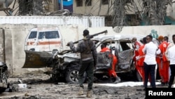 Seorang petugas polisi berjaga-jaga saat pekerja Bulan Sabit Merah mengeluarkan jenazah korban di lokasi ledakan bom mobil bunuh diri di dekat kediaman presiden, di Mogadishu, Somalia, 25 September 2021. (Foto: Reuters)