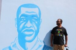 Ruhel Islam, owner of Gandhi Mahal Restaurant, poses next to a mural of George Floyd located across the street from the ruins of the restaurant. Despite losing his restaurant, Islam continues to support the Black Lives Matter movement. (K. Khan/VOA)