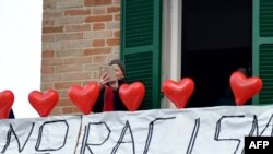 Une femme sur son balcon où elle a mis des ballons rouges portant le nom des victimes et une banderole disant "non au racisme" lors d'une manifestation antiraciste dans la ville de Macerata, en Italie, le 10 février 2018.
