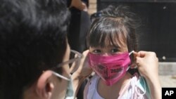 FILE - In this June 10, 2020, file photo, Olivia Chan's father helps her with a new mask she received during a graduation ceremony for her Pre-K class in front of Bradford School in Jersey City, N.J. (AP Photo/Seth Wenig, File)