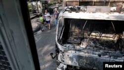 Orang melewati kendaraan yang dibakar di tempat bentrokan antara pemrotes dan polisi di Bangkok, Thailand, 7 Desember 2013. 