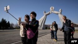 FILE - Tourists from China pose for photos before the Three Charters monument in Pyongyang, April 15, 2019. North Korea will ban foreign tourists to protect itself against a new virus, a major tour operator said Jan. 22, 2020.